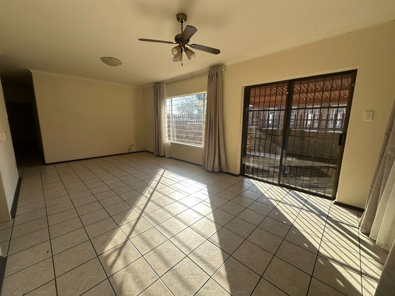 A spacious, empty living room featuring tiled flooring, a ceiling fan, and a sliding glass door with security gate leading to the exterior.