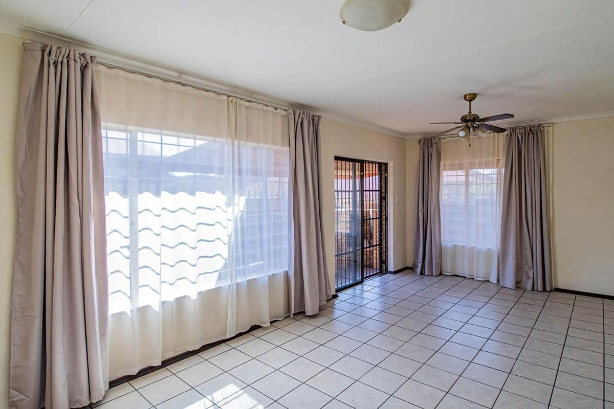 Spacious living area featuring neutral tiled flooring, a ceiling fan, and large windows with sliding door access to the exterior.