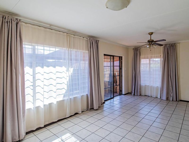 Spacious living area featuring neutral tiled flooring, a ceiling fan, and large windows with sliding door access to the exterior.
