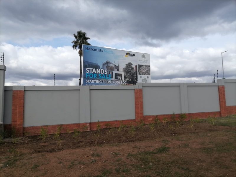 A view of the residential development site featuring a secure perimeter wall with electric fencing and a large promotional billboard.