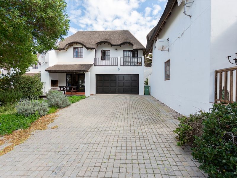 Front elevation of a two-story house featuring a thatched roof, paved driveway, integrated garage, and a balcony.