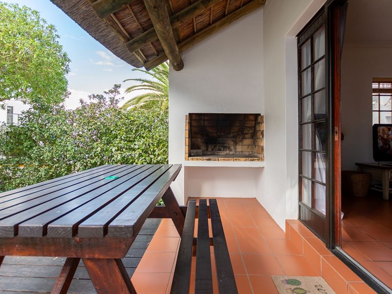 Covered patio area featuring a built-in braai, tiled flooring, and a thatched roof, providing direct access to the interior living space.