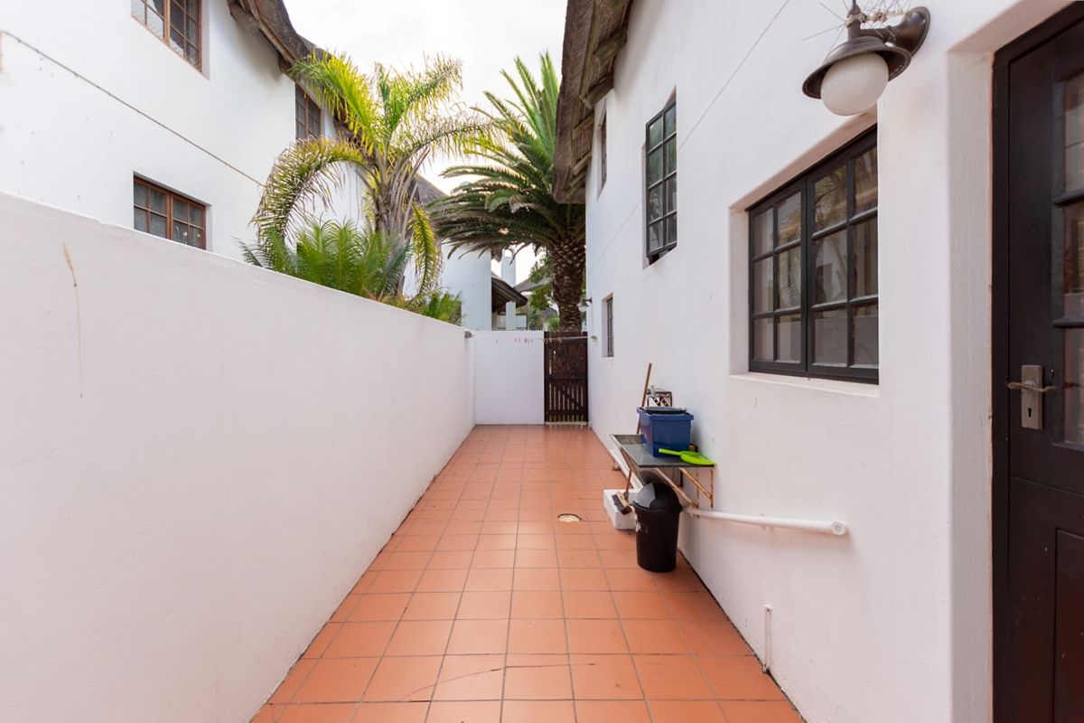 A narrow exterior side passage featuring tiled flooring, boundary walls, and access to the rear garden area.