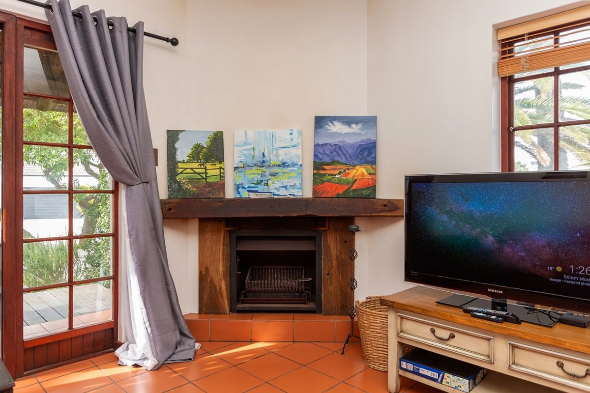 A cozy living room featuring a corner fireplace with a timber mantelpiece, terracotta floor tiles, and direct access to an outdoor area.