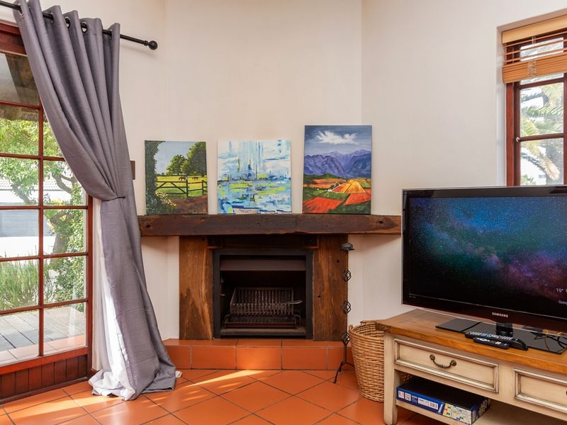 A cozy living room featuring a corner fireplace with a timber mantelpiece, terracotta floor tiles, and direct access to an outdoor area.