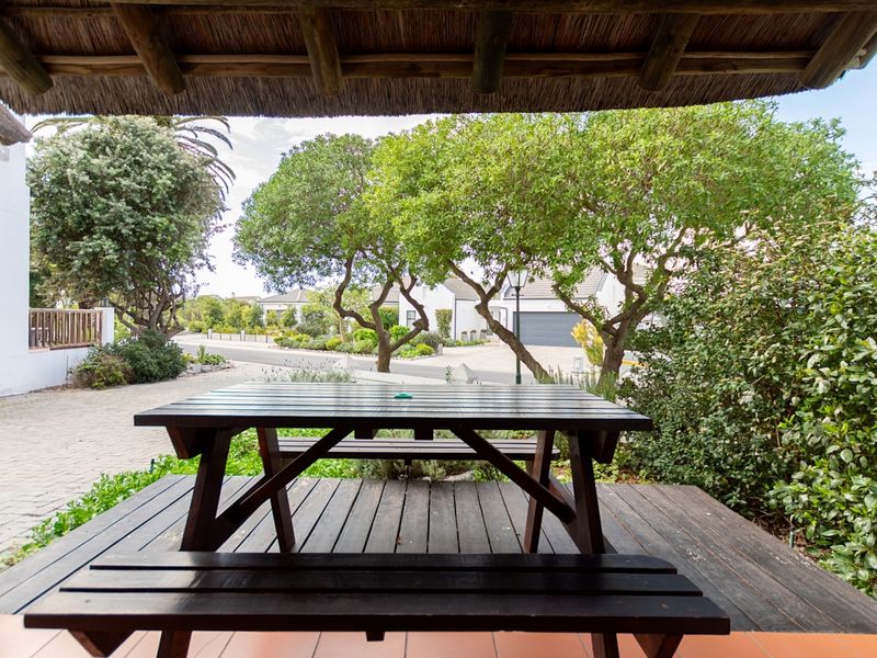 A covered patio area featuring a thatched roof and timber decking, overlooking a landscaped garden and paved driveway.
