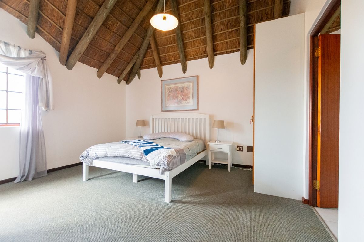 A bedroom featuring a high vaulted ceiling with exposed timber rafters and thatch, carpeted flooring, and a built-in cupboard.