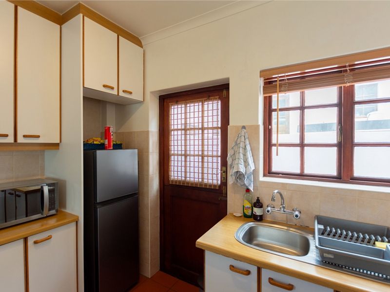 A functional kitchen featuring laminate countertops, built-in cabinetry, a stainless steel sink, and a timber door leading to the exterior.