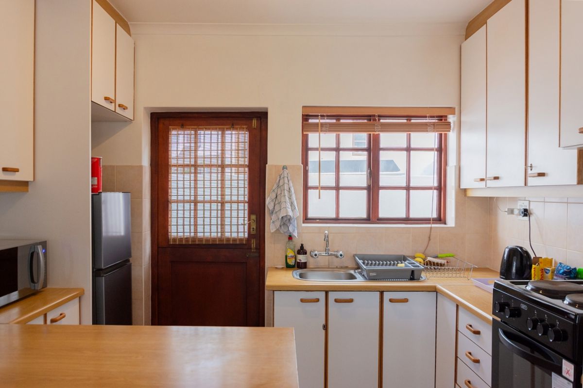 A functional kitchen featuring laminate countertops, built-in cabinetry, a stainless steel sink, and a timber-framed door leading to the exterior.