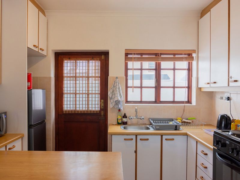 A functional kitchen featuring laminate countertops, built-in cabinetry, a stainless steel sink, and a timber-framed door leading to the exterior.