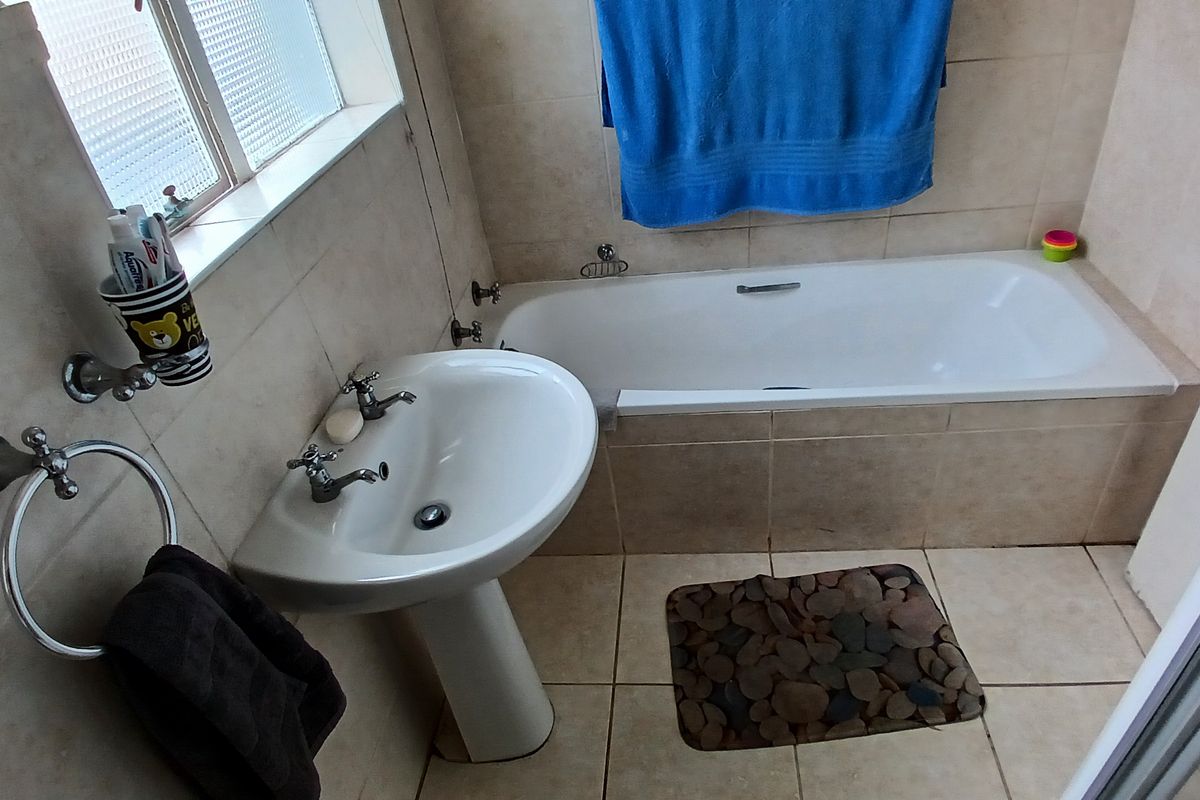 A functional bathroom featuring a pedestal basin, built-in bathtub, and neutral ceramic tiling throughout.