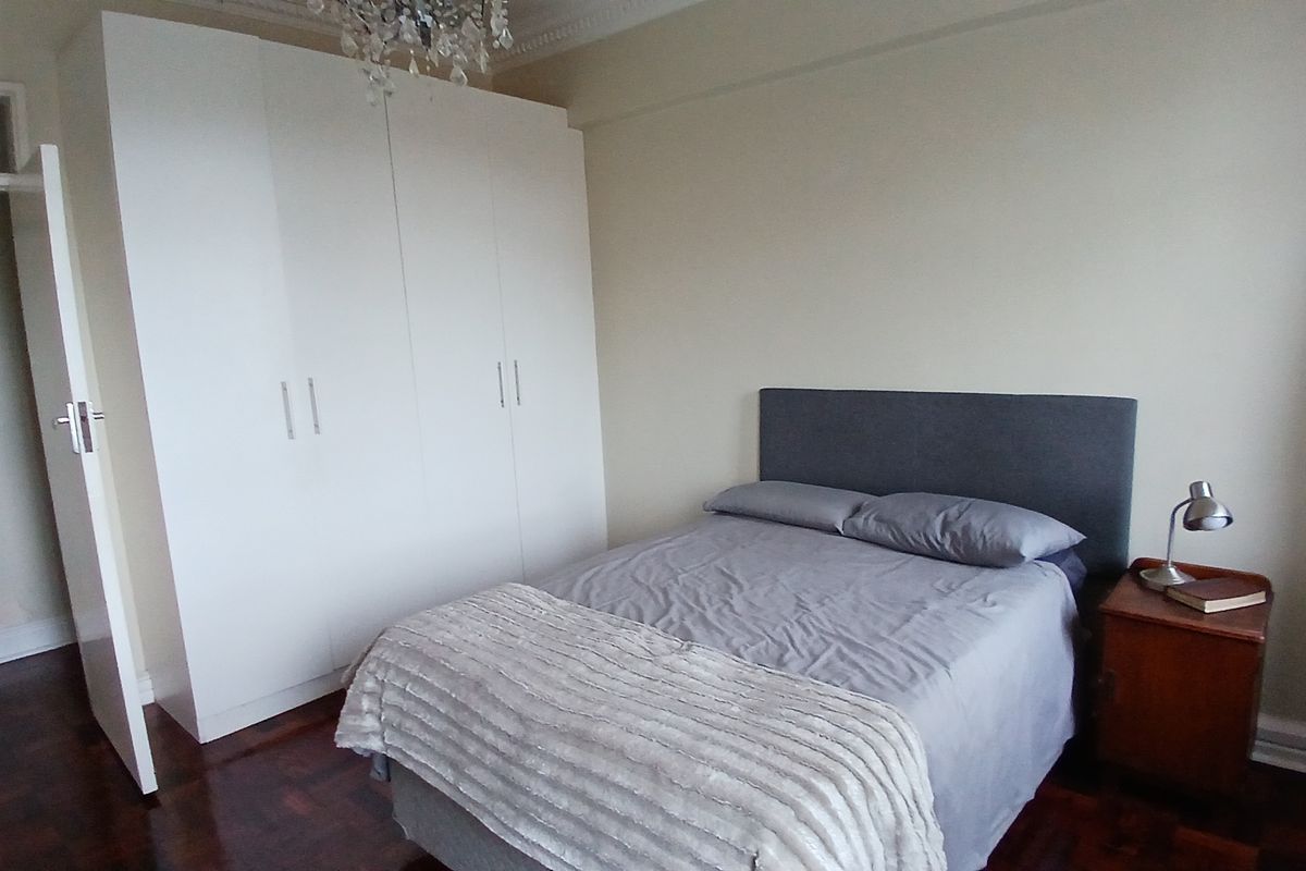 A well-maintained bedroom featuring classic parquet flooring, a large built-in wardrobe, and decorative ceiling cornice.