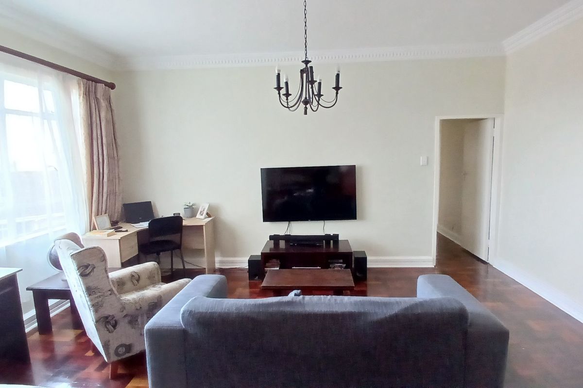 A spacious living room featuring classic parquet flooring, elegant crown molding, and a central chandelier, offering a bright and comfortable living space.