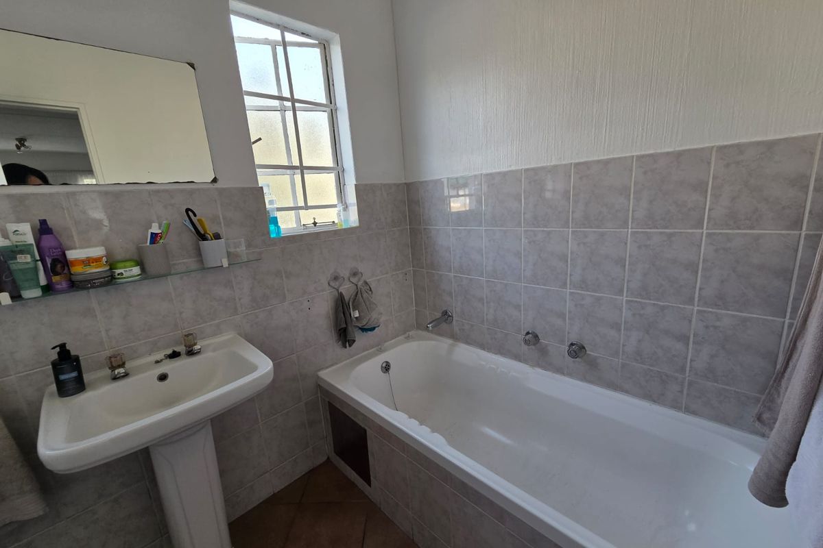 A functional bathroom featuring a pedestal basin, a built-in bathtub with tiled surround, and tiled flooring, offering a classic layout ready for modernization.