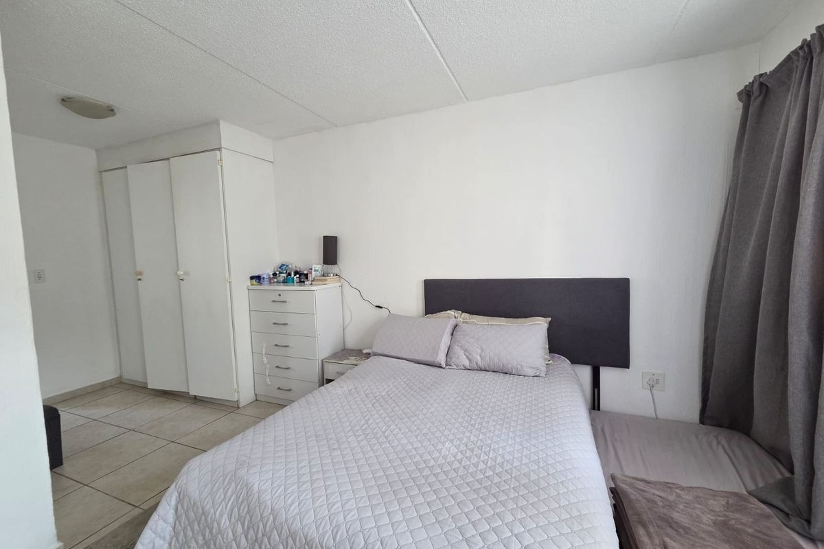 A functional bedroom featuring built-in cupboards, tiled flooring, and neutral wall finishes, providing a clean and practical living space.