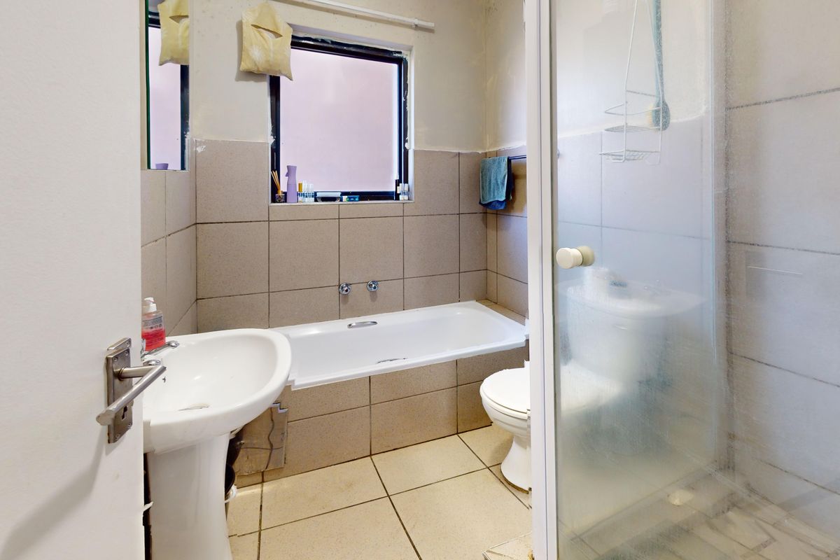 A functional bathroom featuring a pedestal basin, built-in bathtub, and a separate shower enclosure with tiled walls and flooring.