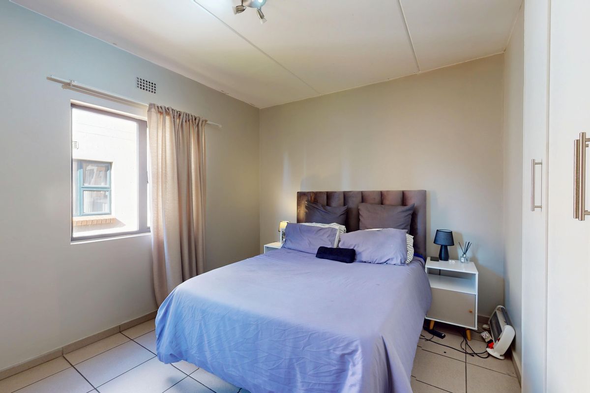 A functional bedroom featuring tiled flooring, a built-in wardrobe, and a window providing natural light.