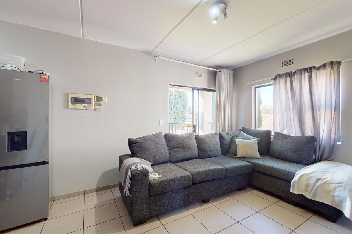 A functional living room featuring tiled flooring, a sliding glass door providing natural light, and a wall-mounted electrical distribution board.