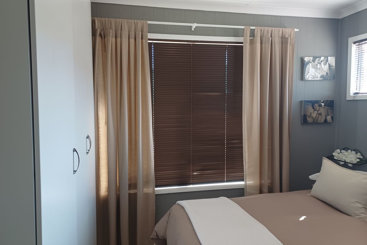 A bedroom featuring a built-in wardrobe and window with venetian blinds, finished with neutral wall tones.
