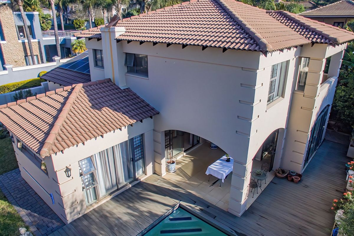 Aerial view of a two-story residential property featuring a tiled roof, a covered patio area, and a swimming pool with surrounding decking.