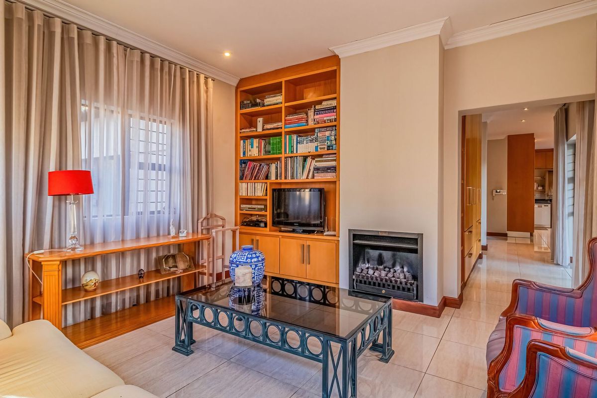 A comfortable living room featuring a built-in wooden shelving unit, a fireplace, and tiled flooring, with a seamless transition to the adjacent kitchen area.