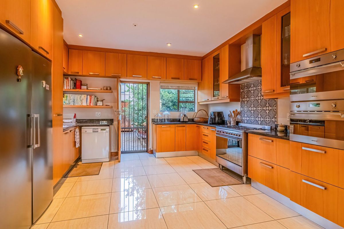 A well-maintained kitchen featuring warm wood cabinetry, granite countertops, integrated stainless steel appliances, and a decorative tiled backsplash with direct access to the exterior.