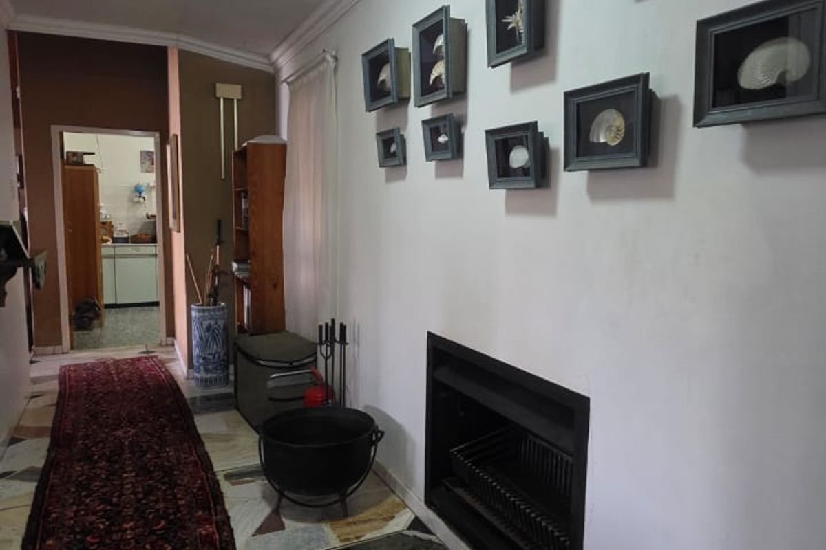 A living area featuring a built-in fireplace, tiled flooring, and decorative ceiling cornices, with a view leading through to an adjacent kitchen space.