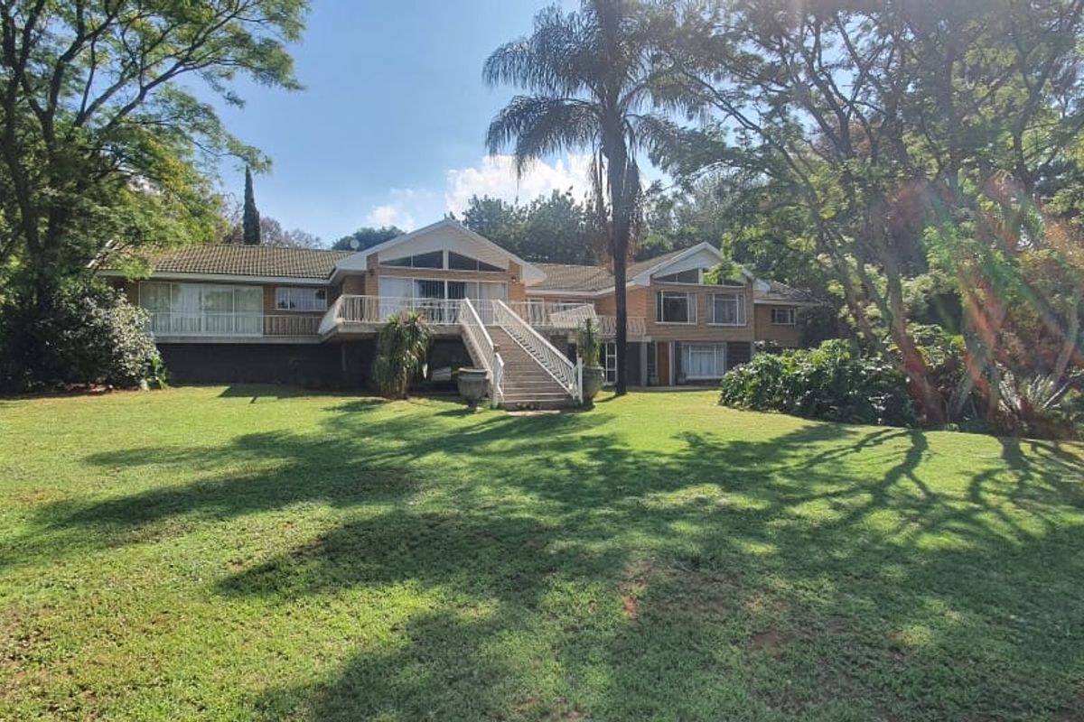 Rear view of a multi-level brick residence featuring a raised deck, external staircase, and expansive landscaped garden surroundings.