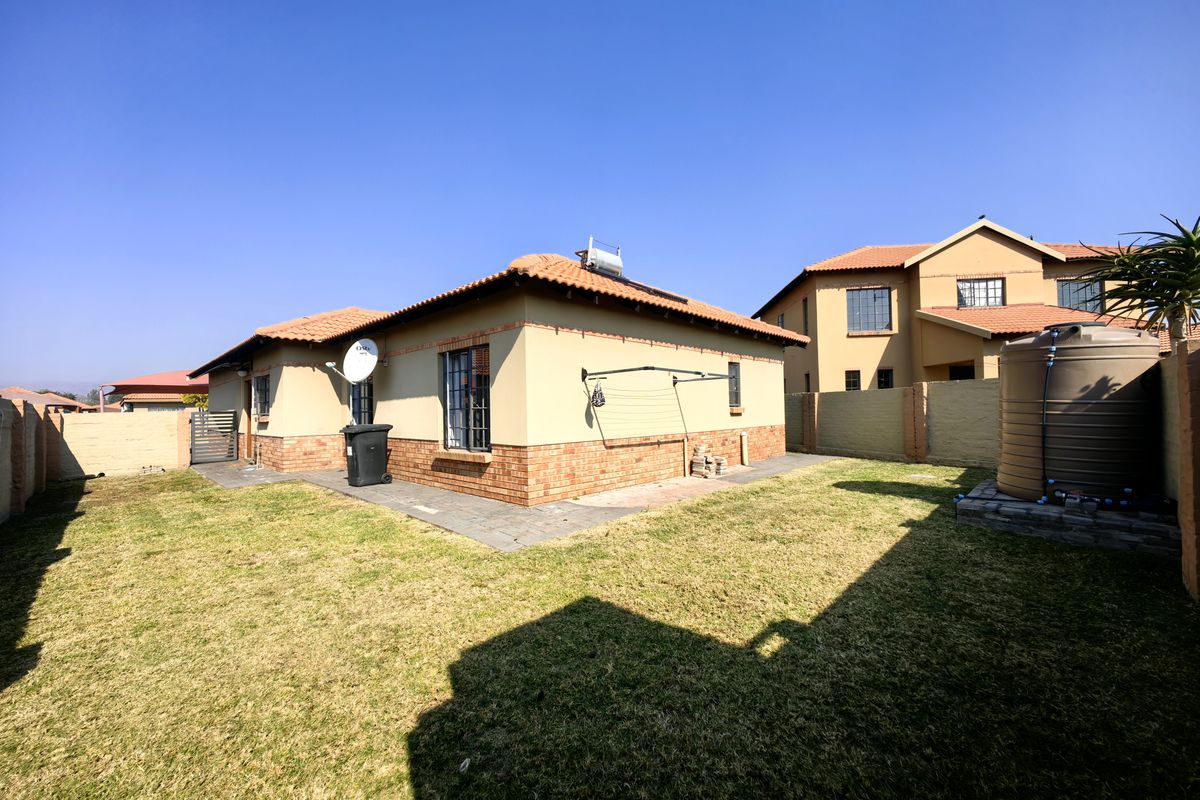Rear view of the property featuring a landscaped garden, paved walkway, solar water heating system, and a large water storage tank.