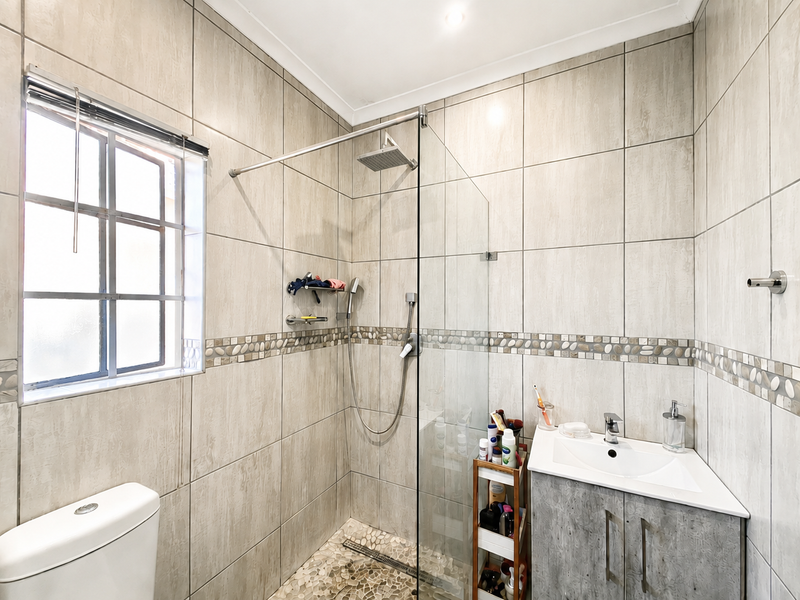 Modern bathroom featuring a walk-in shower with glass screen, rain shower head, vanity unit with basin, and neutral wall tiling.