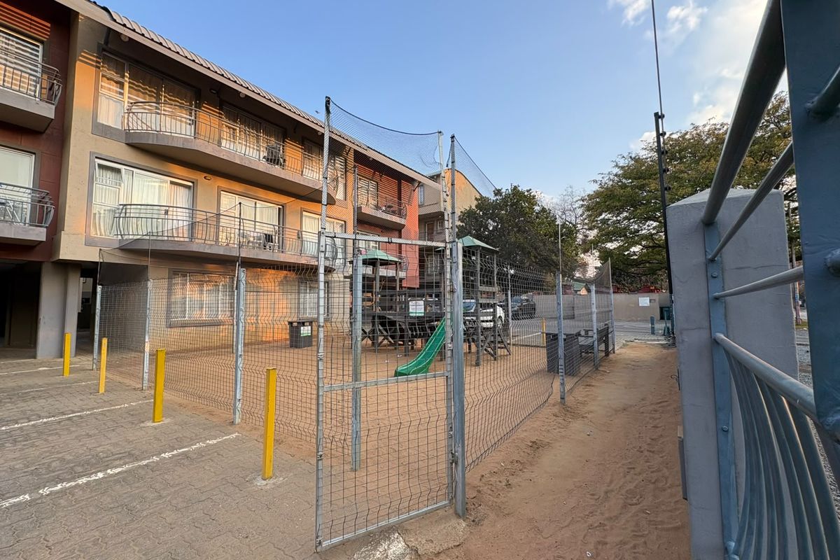 Exterior view of an apartment complex featuring a fenced playground area, paved parking, and multiple balconies with sliding door access.