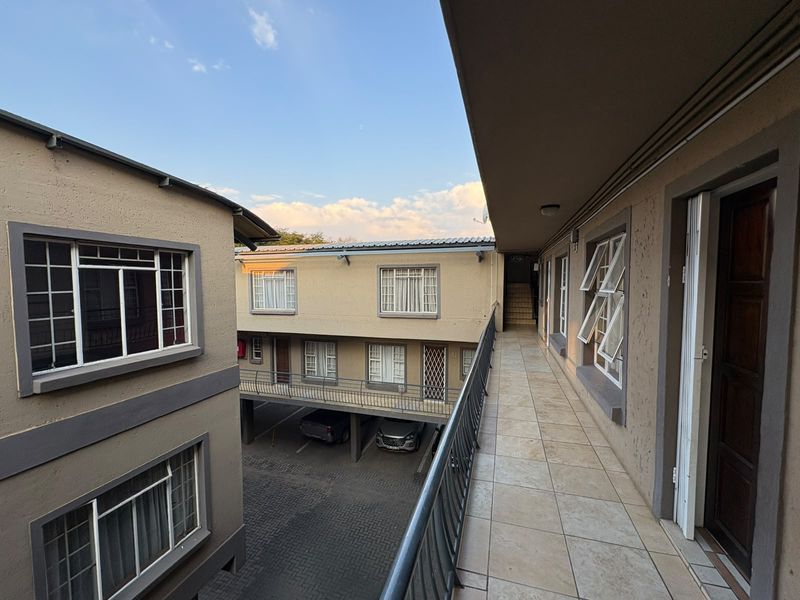 An exterior view of an apartment complex walkway featuring tiled flooring, metal balustrades, and access to multiple residential units.