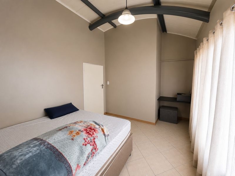 A bedroom featuring tiled flooring, exposed ceiling beams, and a built-in shelving unit, offering a neutral canvas for interior design.