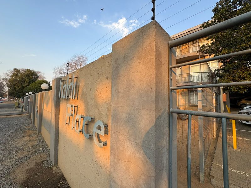 Exterior view of the apartment complex entrance featuring a perimeter wall with electric fencing and building signage.