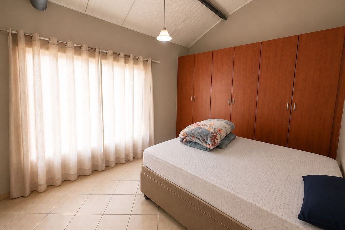 A well-lit bedroom featuring vaulted ceilings, neutral tiled flooring, and extensive built-in wooden cabinetry for storage.