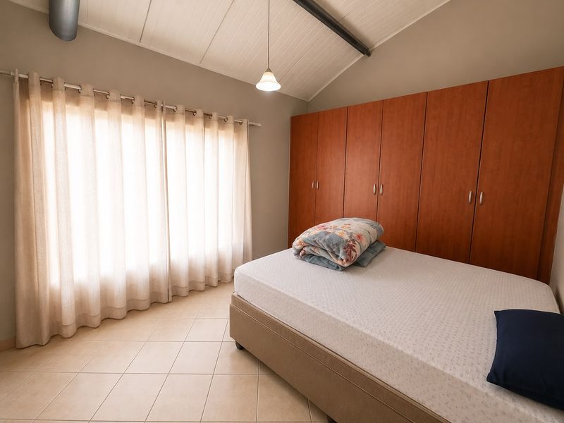 A well-lit bedroom featuring vaulted ceilings, neutral tiled flooring, and extensive built-in wooden cabinetry for storage.