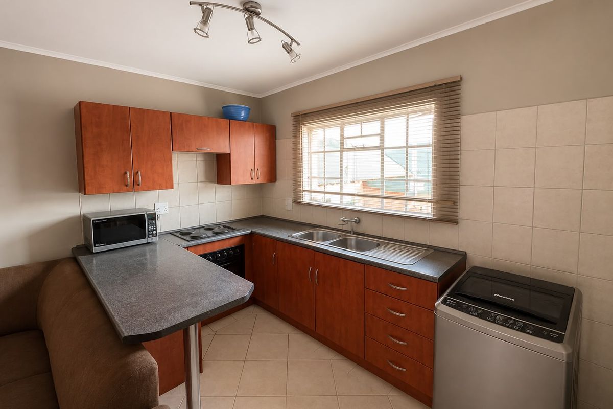 A functional kitchen featuring wood-finish cabinetry, laminate countertops, a double sink, and built-in cooking appliances with tiled splashbacks and flooring.