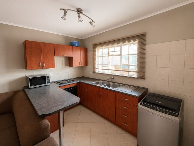 A functional kitchen featuring wood-finish cabinetry, laminate countertops, a double sink, and built-in cooking appliances with tiled splashbacks and flooring.