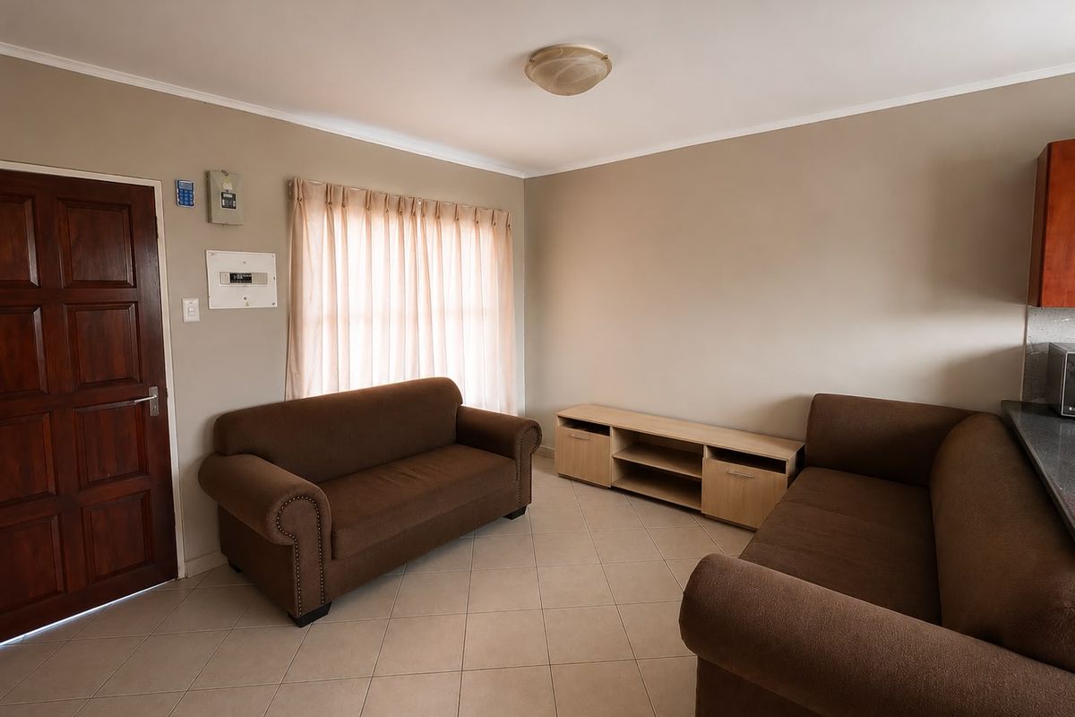 A functional living room featuring tiled flooring, neutral wall tones, and a solid wood entrance door, providing a comfortable and practical living space.