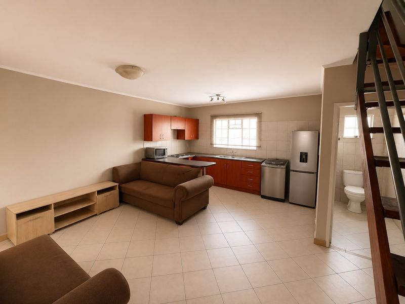 Open-plan living area featuring a functional kitchen with built-in cabinetry, tiled flooring, and an adjacent bathroom, with a staircase leading to the upper level.