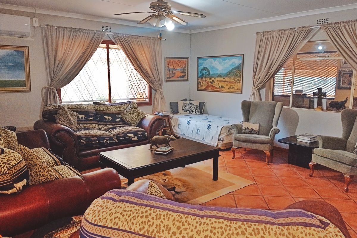 A spacious living room featuring tiled flooring, a ceiling fan, and an air conditioning unit, with large windows fitted with security bars.