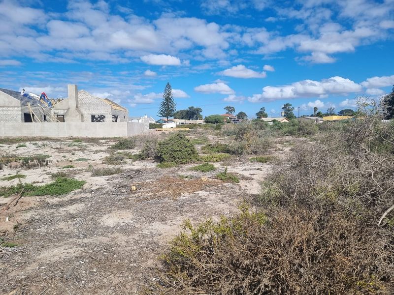 A vacant plot of land featuring natural vegetation with a partially constructed masonry building and chimney stack visible in the background.