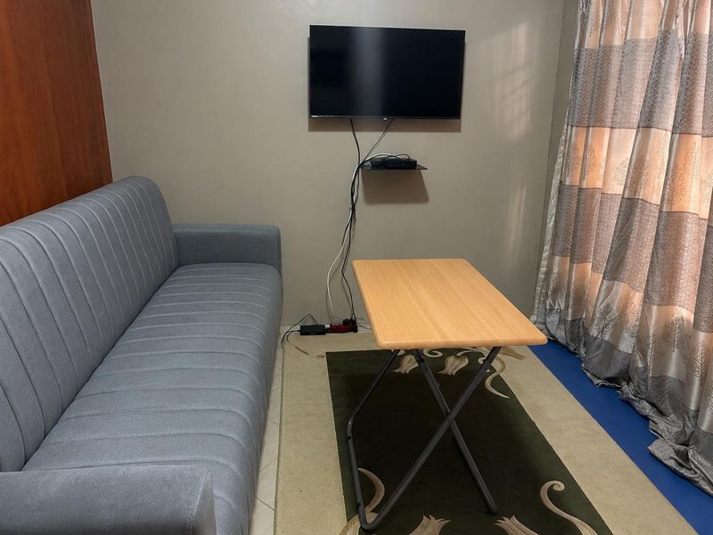 A compact living area featuring a wall-mounted television and neutral wall finishes, suitable for a small apartment layout.