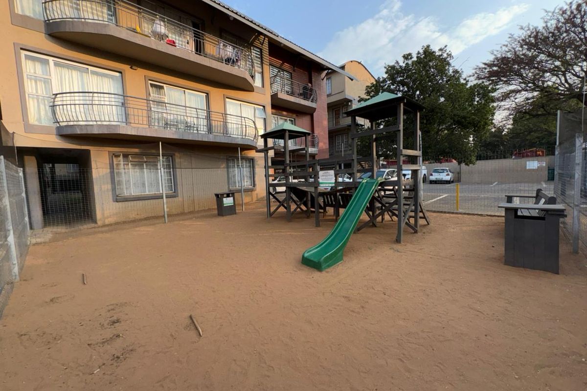 Rear exterior view of the apartment complex featuring a communal playground area with slide and metal perimeter fencing.