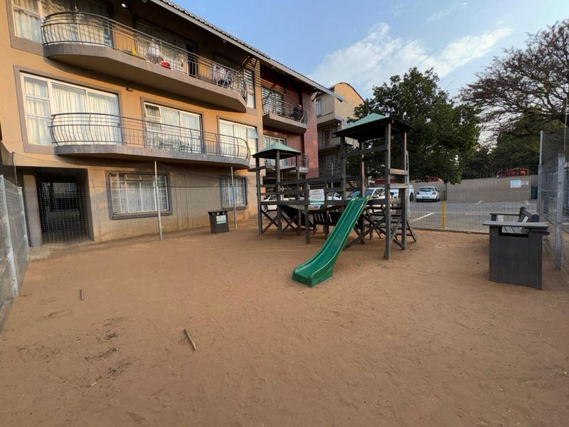 Rear exterior view of the apartment complex featuring a communal playground area with slide and metal perimeter fencing.