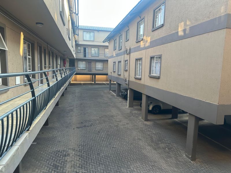 View of the apartment complex exterior featuring a paved driveway, covered parking bays, and external access walkways with metal balustrades.