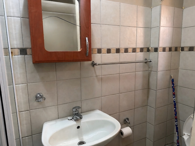 A functional bathroom featuring a wall-mounted basin, chrome fixtures, and tiled walls, currently requiring maintenance due to a cracked mirror.
