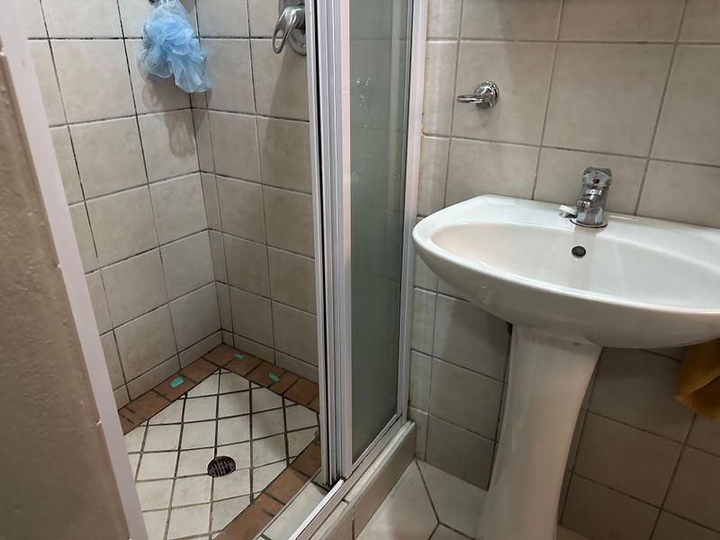 A compact bathroom featuring a pedestal basin and a separate shower enclosure with tiled finishes, requiring some maintenance and cosmetic updates.