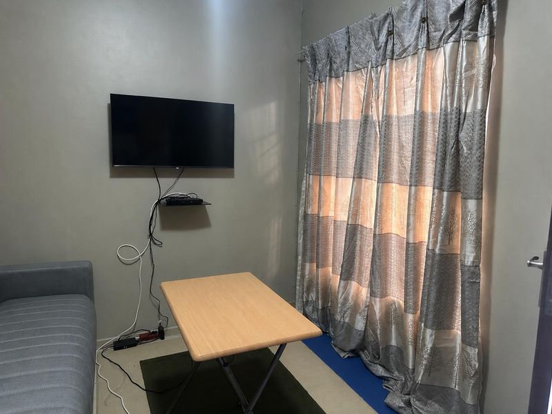 A compact living area featuring a wall-mounted television and large window curtains, providing a functional space for relaxation.