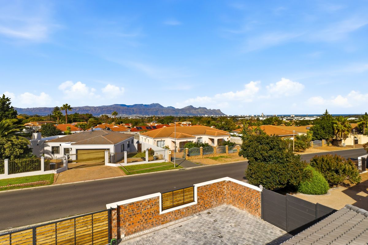 An elevated aerial view of the residential neighborhood, showcasing the property's exterior, paved driveway, boundary walls, and surrounding suburban landscape with mountain views.